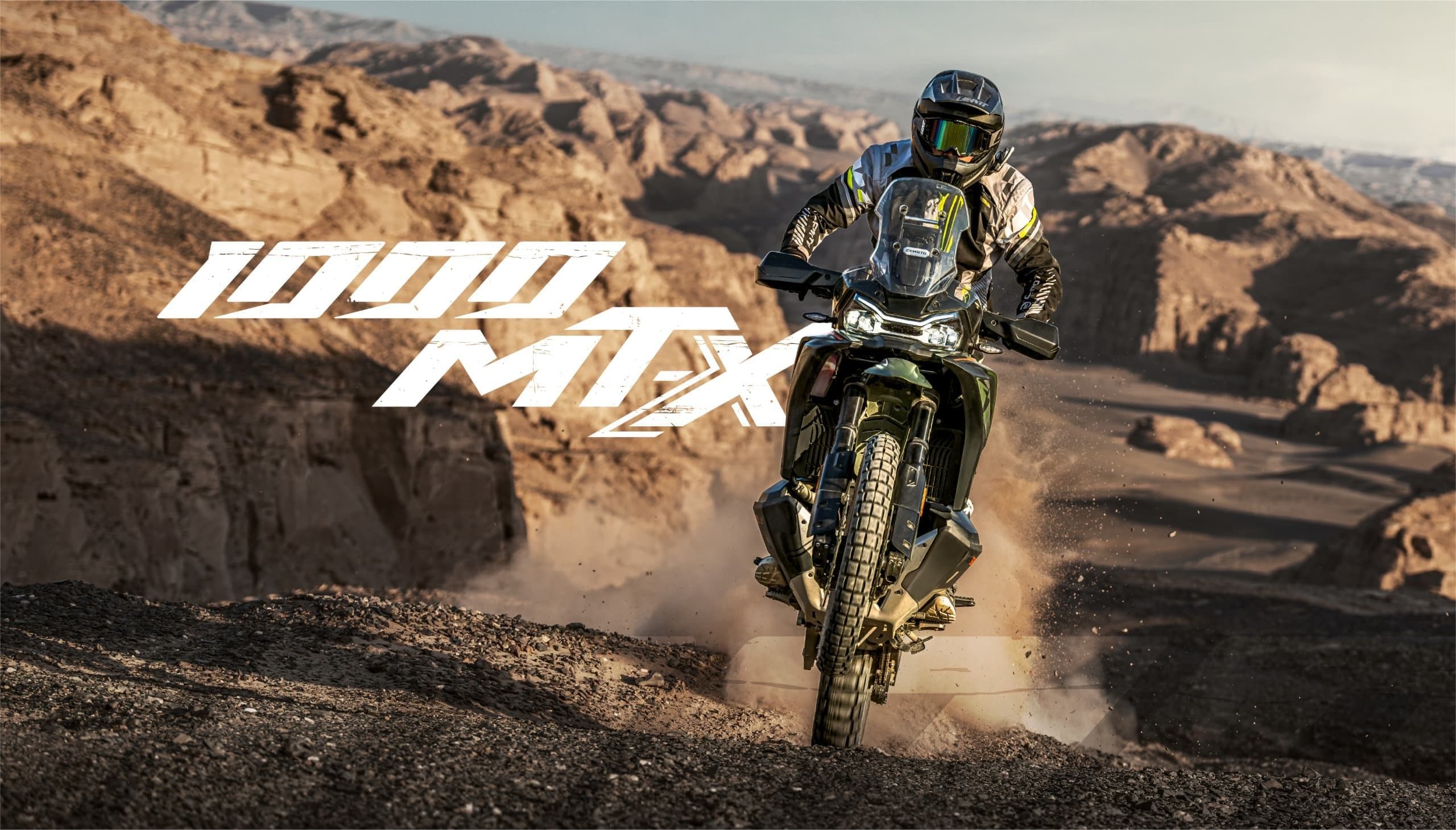 An adventure motorcycle with "1000 MTX" text rides through a rugged, arid desert environment.