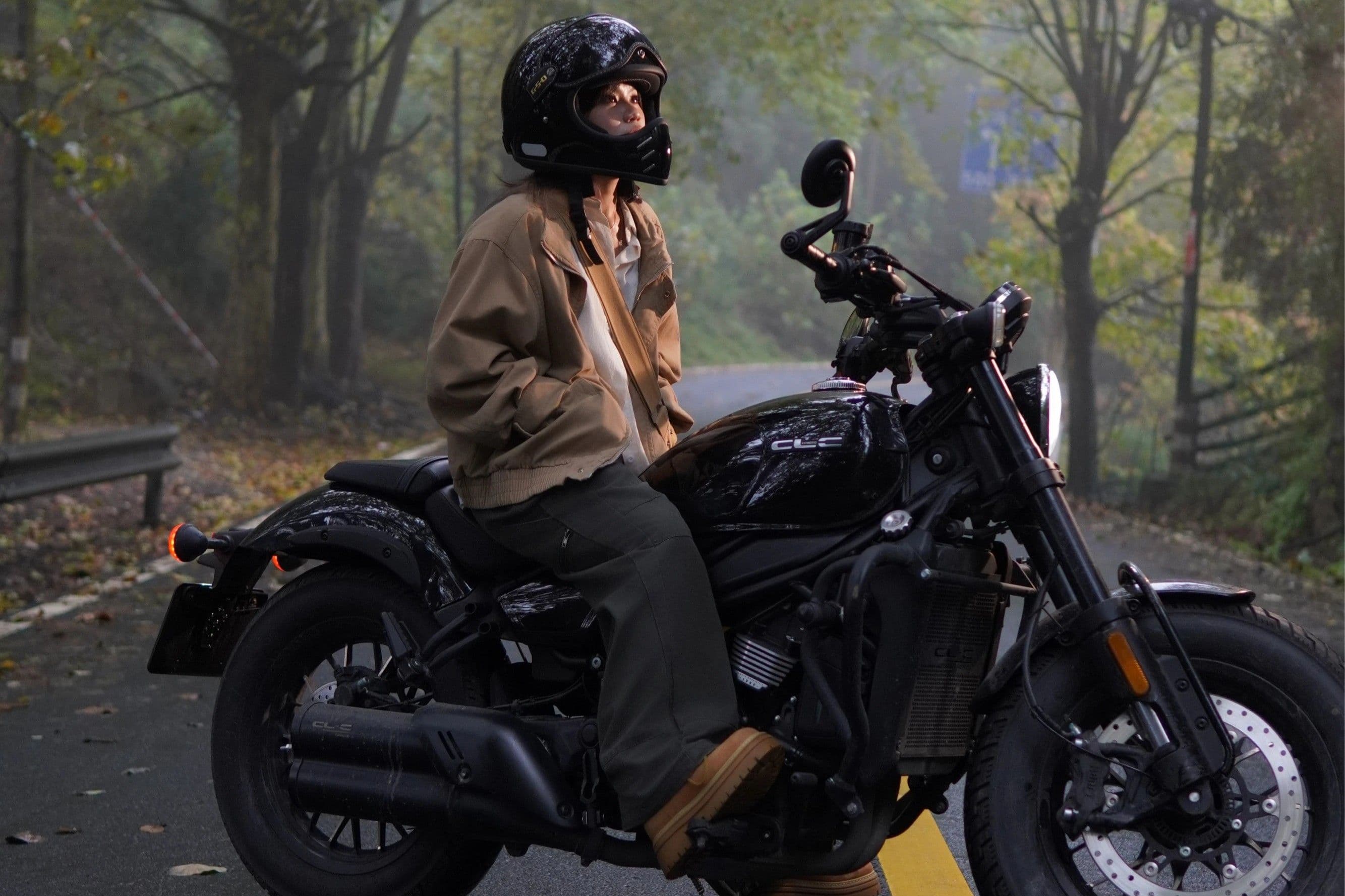 Person in a dark helmet and brown jacket sitting on a black motorcycle.