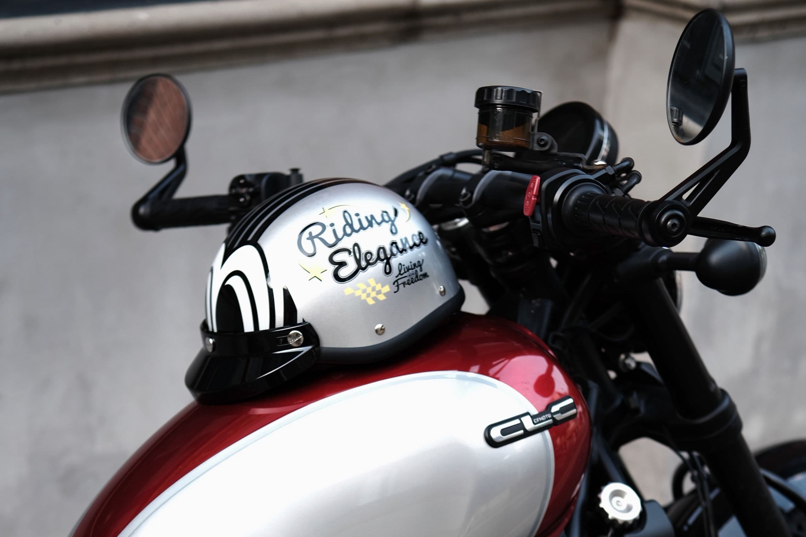 Silver motorcycle helmet with "Riding Elegance" on a red and silver fuel tank.