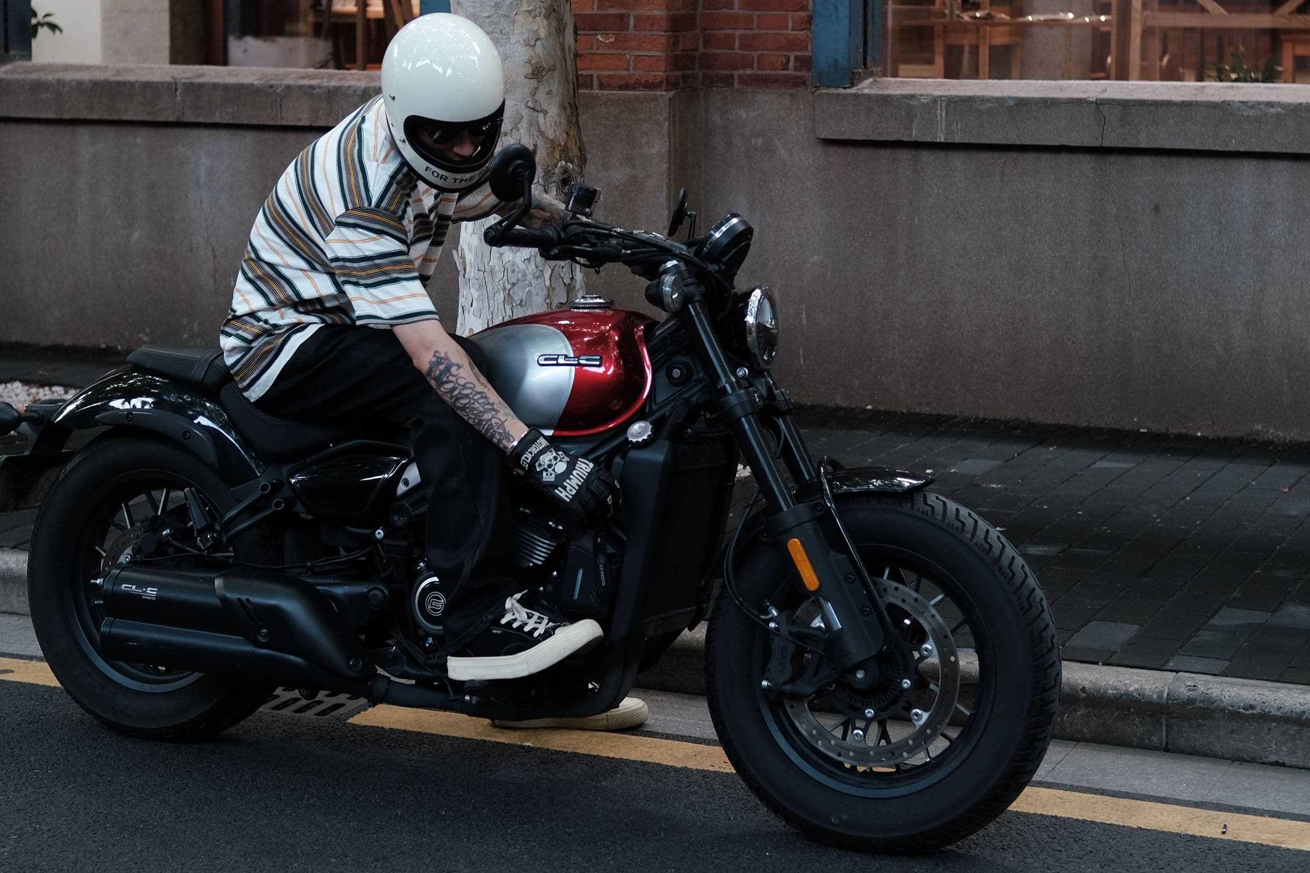 Man in a white helmet and striped shirt rides a black motorcycle.