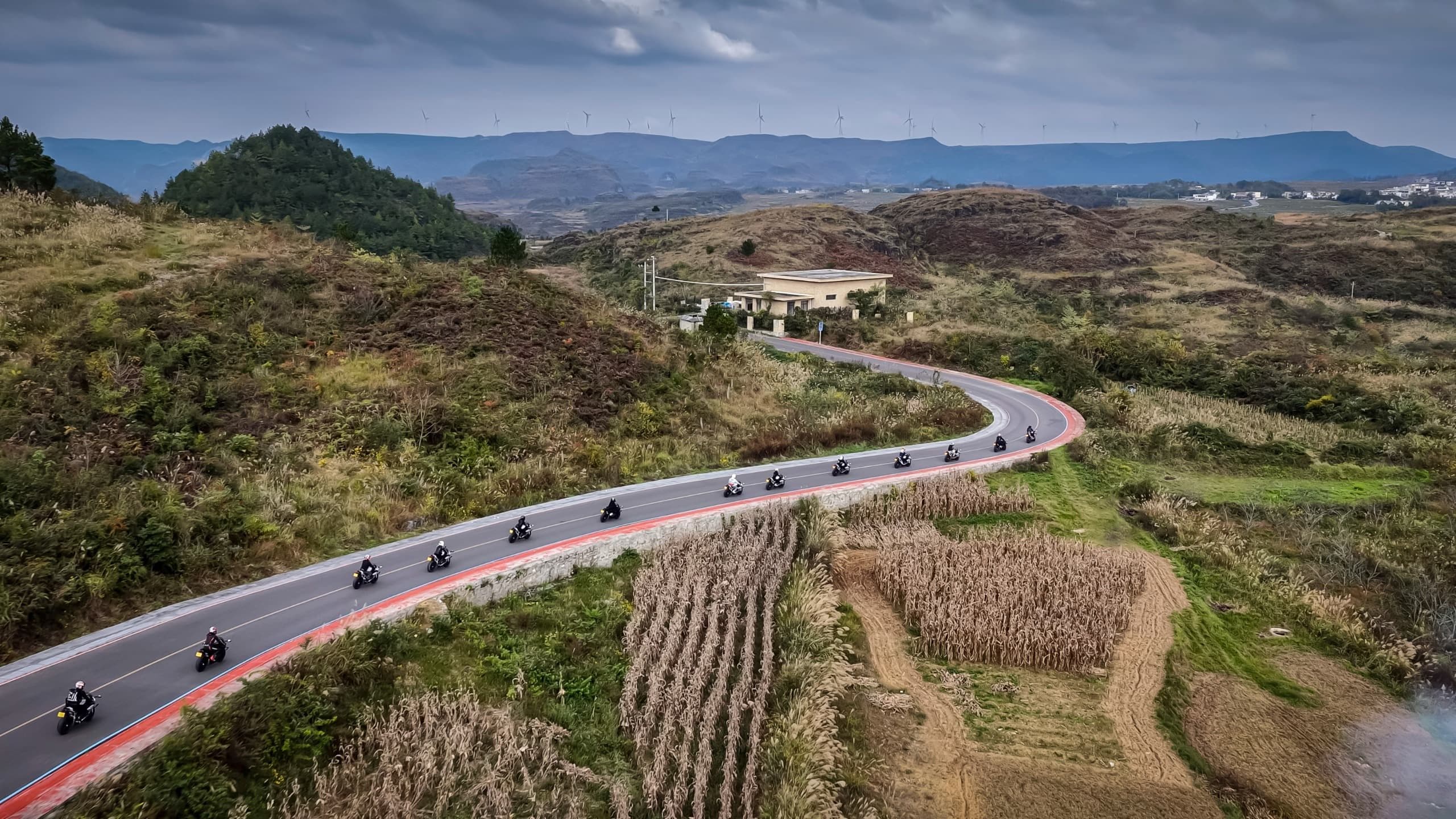 Aerial view of motorcyclists on a long winding road through fields and distant hills.