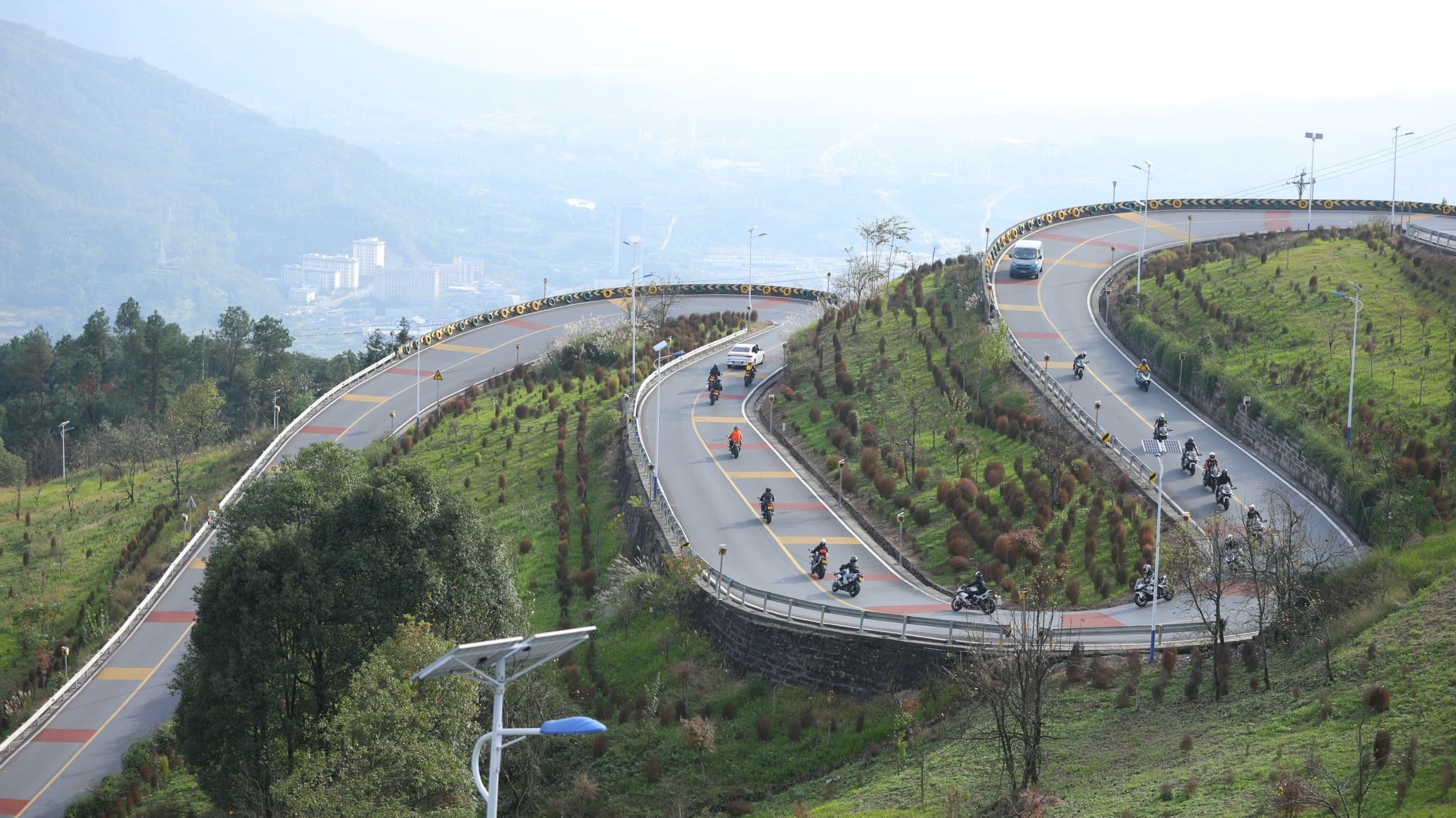 Winding mountain road with vehicles traversing multiple curves amidst green slopes.