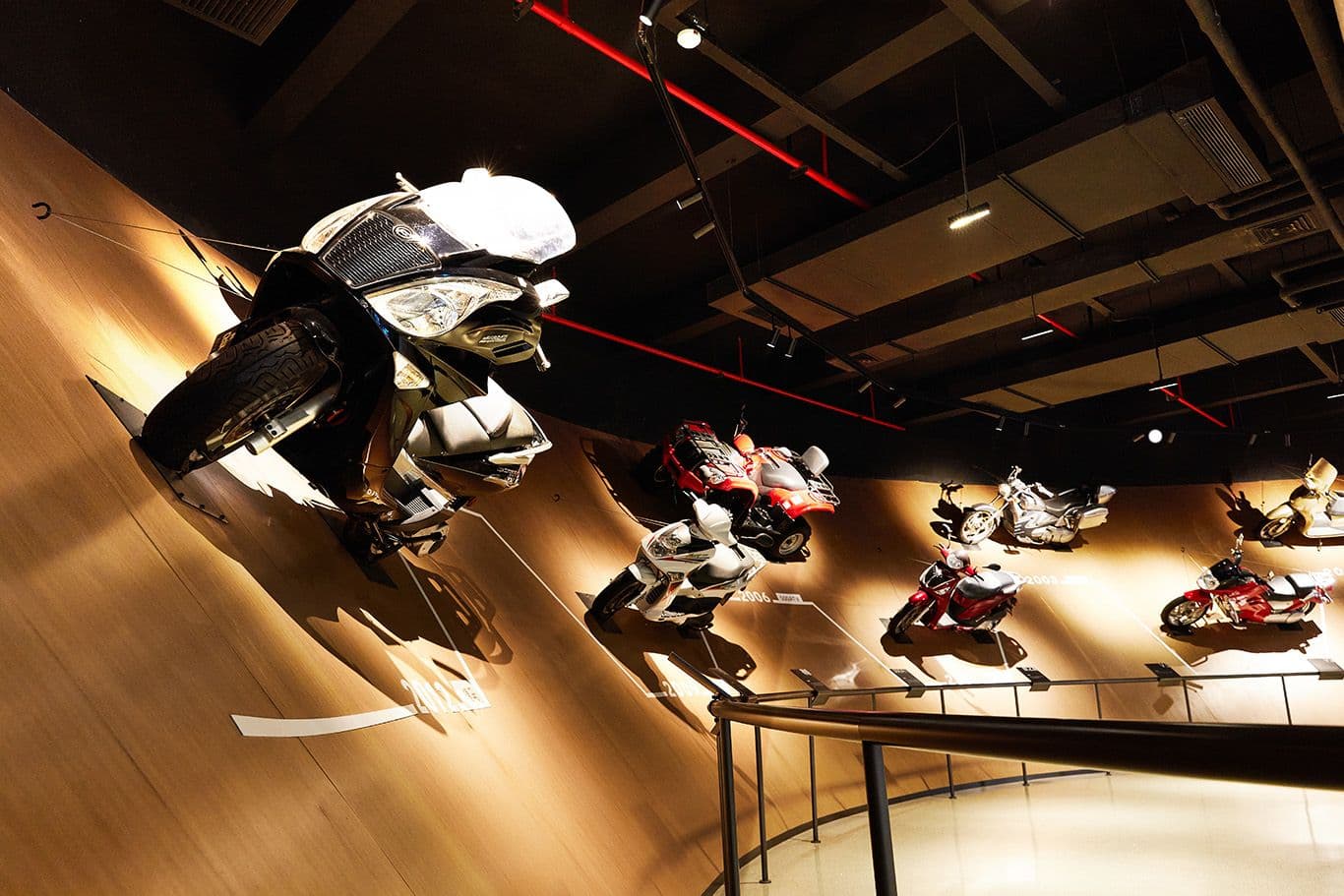 Mannequins in racing suits on motorcycles mounted dynamically on a curved wooden wall display.