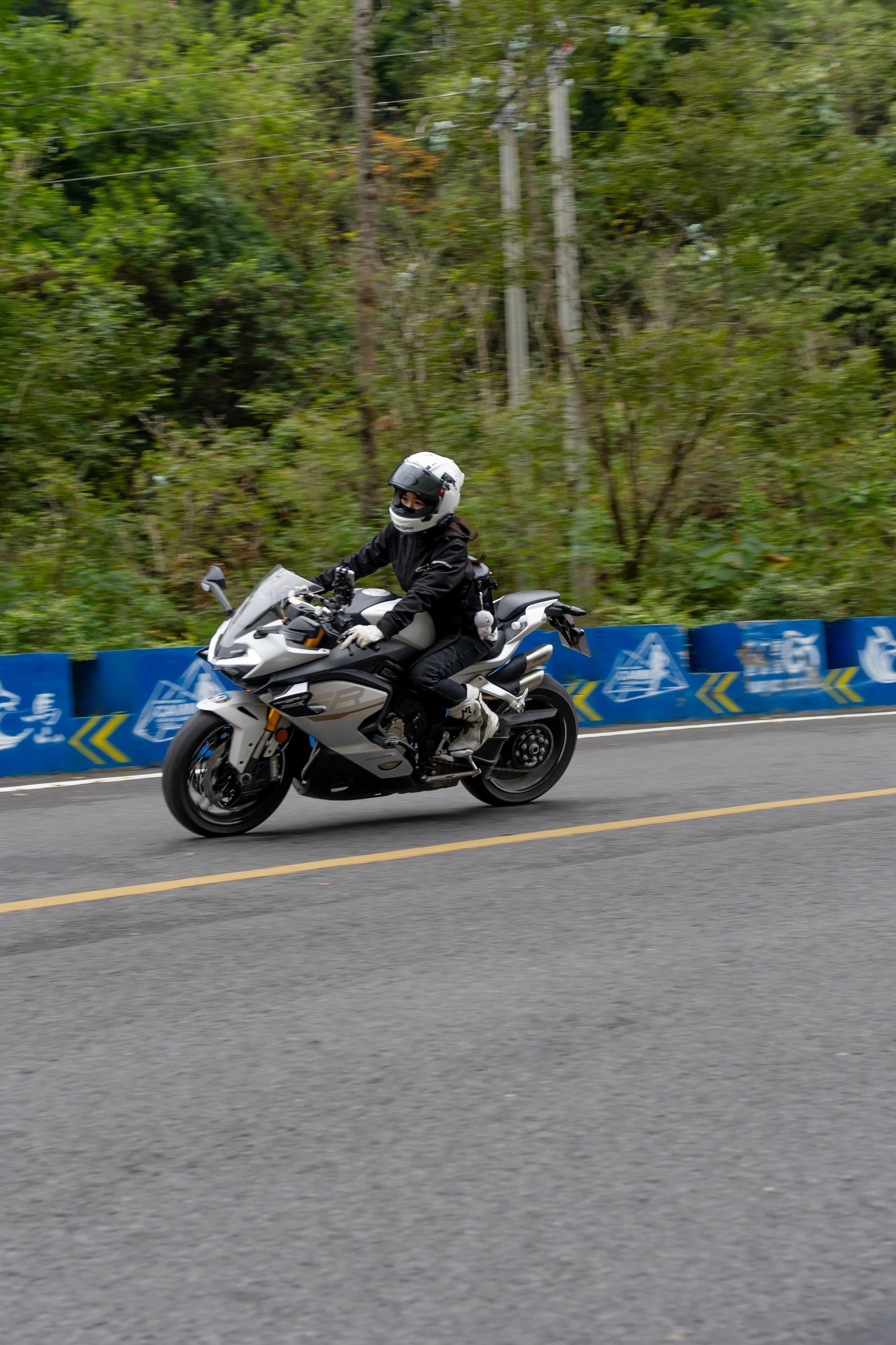 A motorcyclist in white and black gear rides a white sport bike on a scenic road.