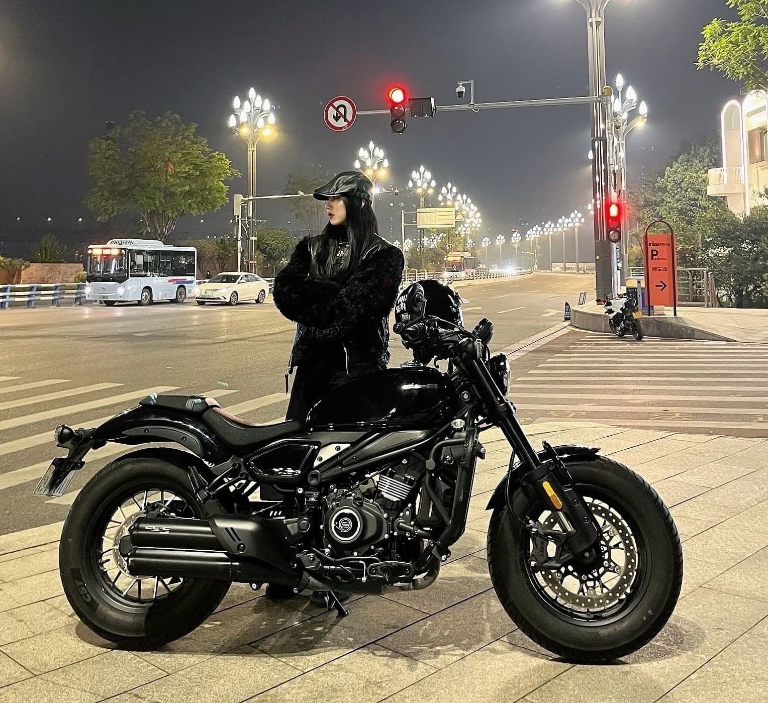 Person in black stands beside a powerful black cruiser motorcycle at night.