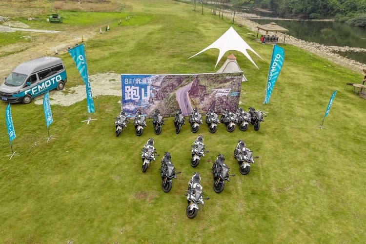 Aerial view of numerous motorcycles parked in formation on a green field next to a CFMOTO van.