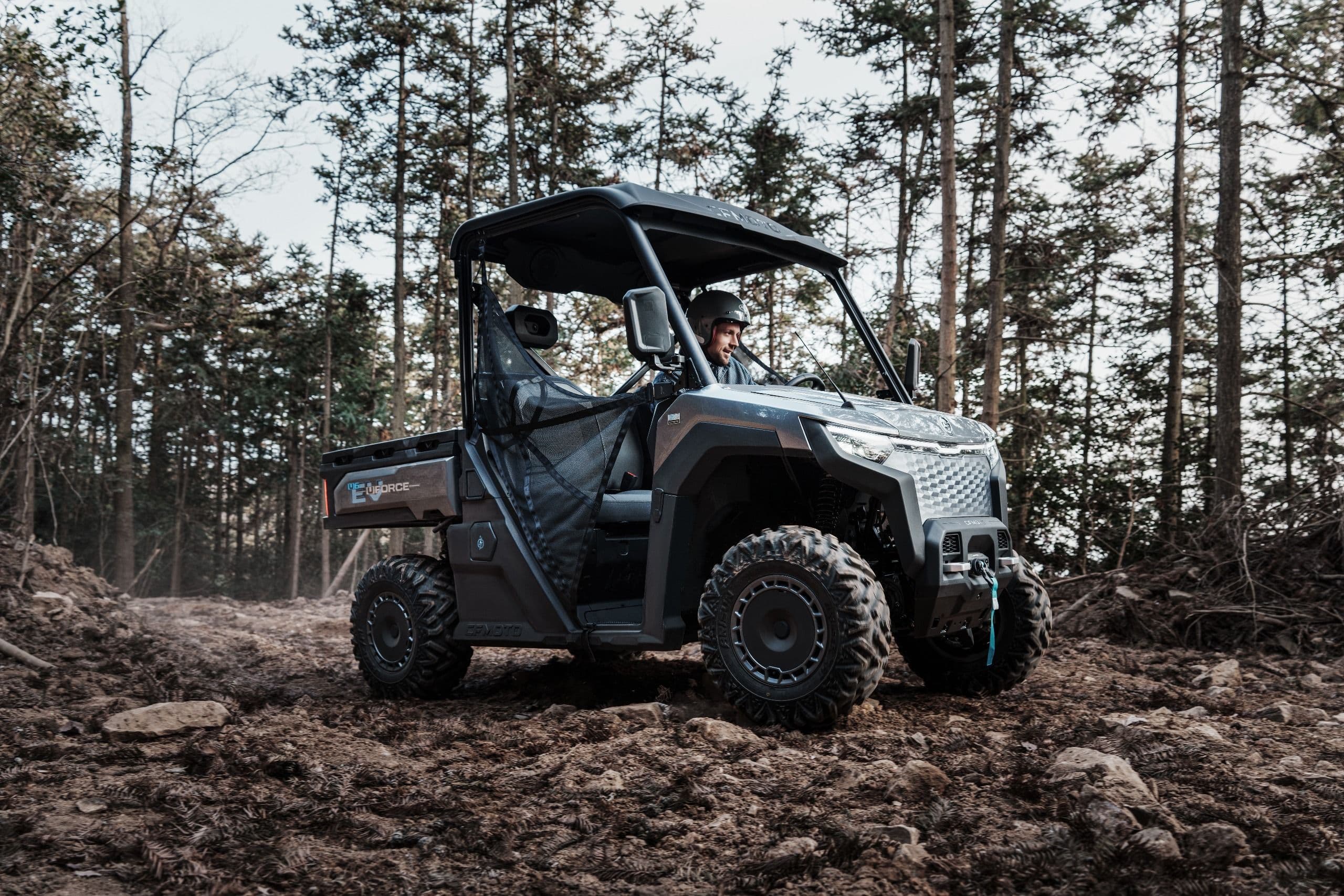 Gray UTV parked on a muddy forest trail surrounded by trees.