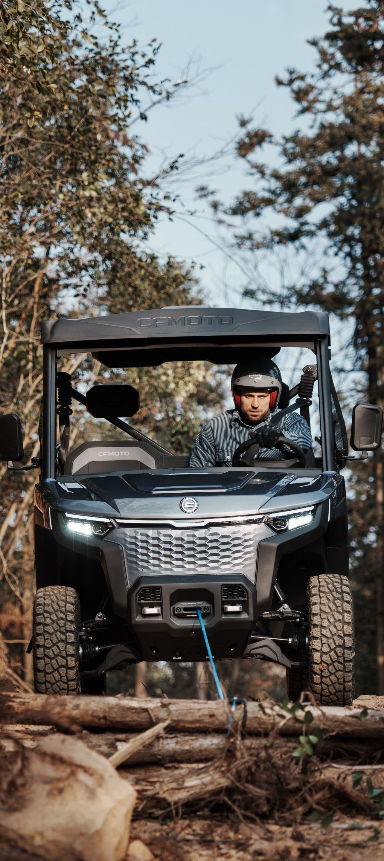 A person in a helmet drives a dark utility vehicle through a rugged, forested trail.